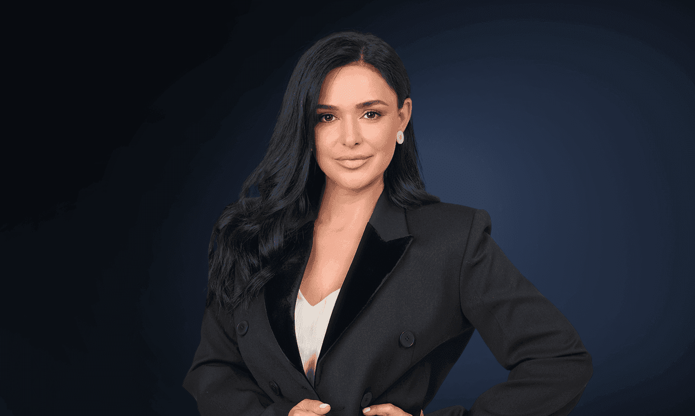 A professional woman with dark hair and a black suit smiles confidently.